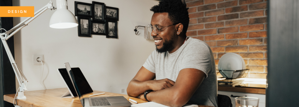 A man sitting at a counter in his kitchen, smiling into a laptop screen as if on a Zoom meeting